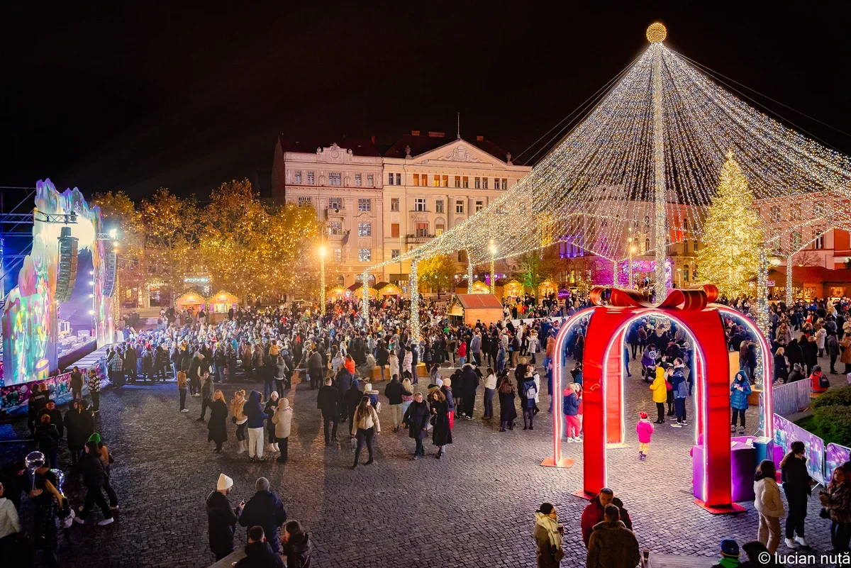 Târgul de Crăciun din Cluj-Napoca - Piața Unirii luminată feeric cu cupola piramidală de lumini, poarta cadou și mulțimea festivă
